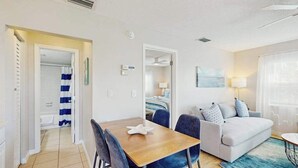 Een moderne woonkamer met een bank, een eettafel met stoelen, een plafondventilator en een raam met gordijnen.