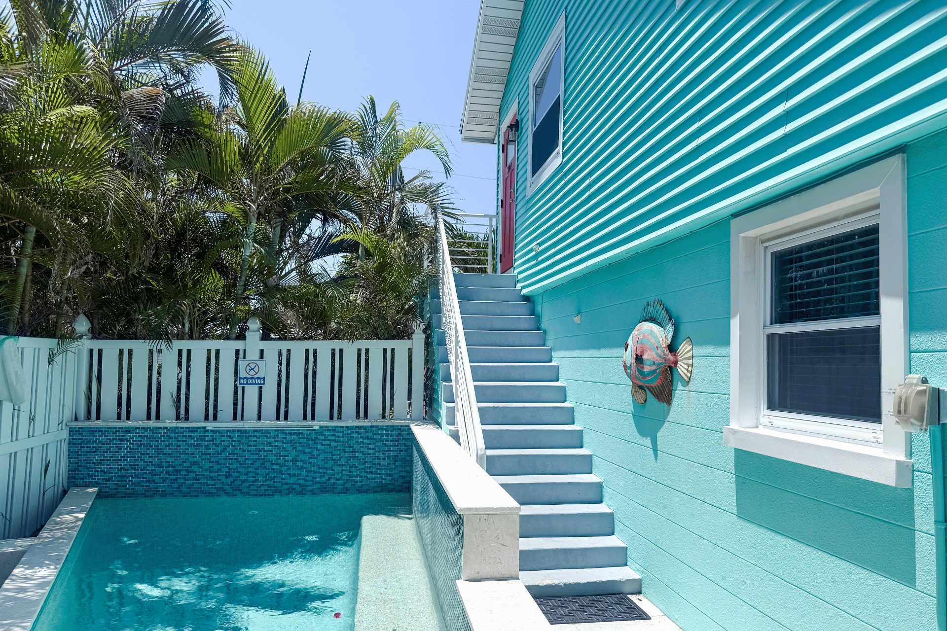 A turquoise building with a pool, a white fence, and a no diving sign.
