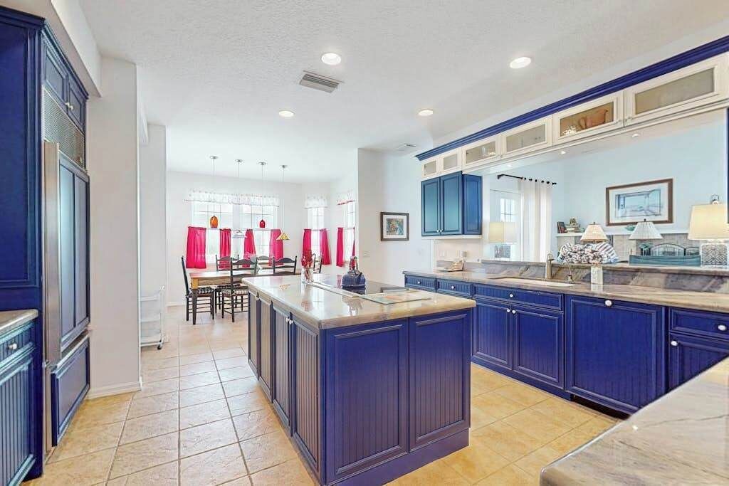 A kitchen with a central island, blue cabinets, and a dining area with red curtains.
