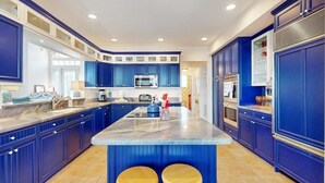 Une cuisine avec des meubles de couleur bleue, un îlot en marbre et deux tabourets.
