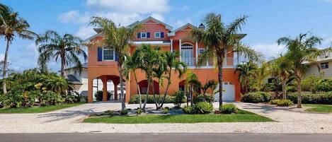 A two-story house with a red facade, a front porch, and palm trees.