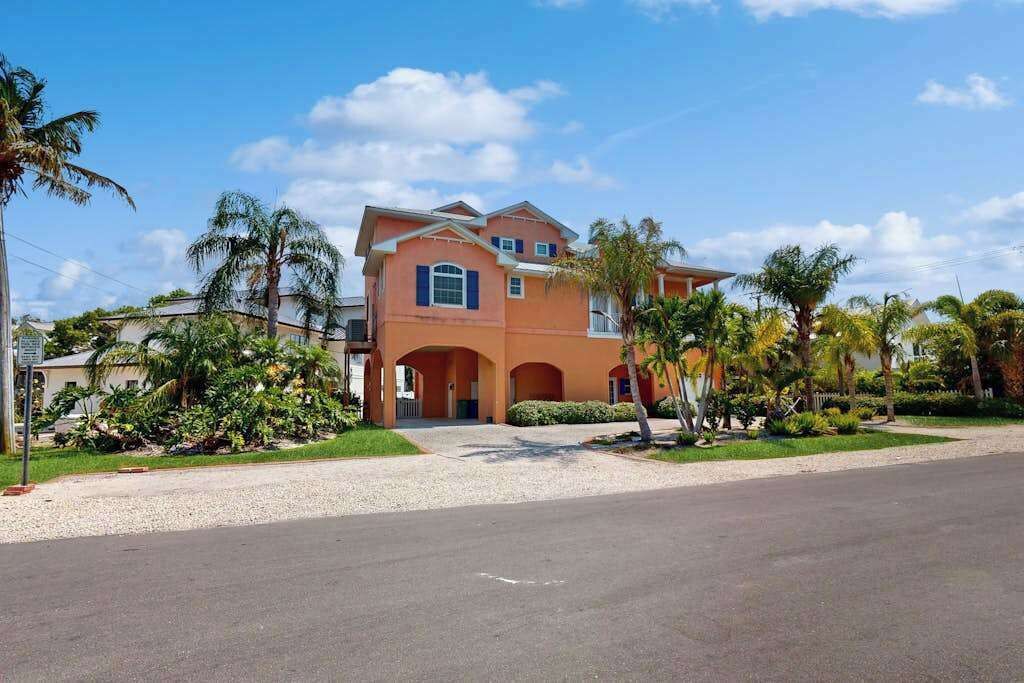 A two-story house with a driveway, surrounded by palm trees and greenery.