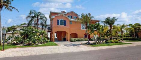 A two-story house with a driveway, surrounded by palm trees and greenery.