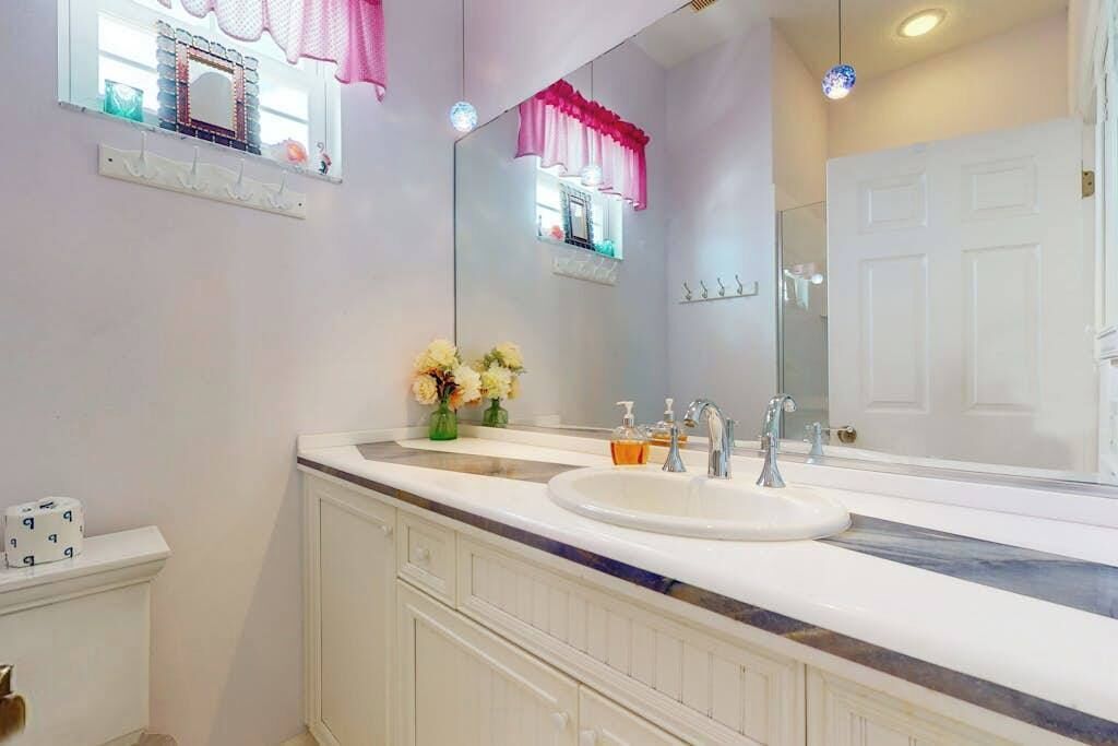 Une salle de bain avec un lavabo blanc, deux miroirs, un meuble-lavabo et une porte.