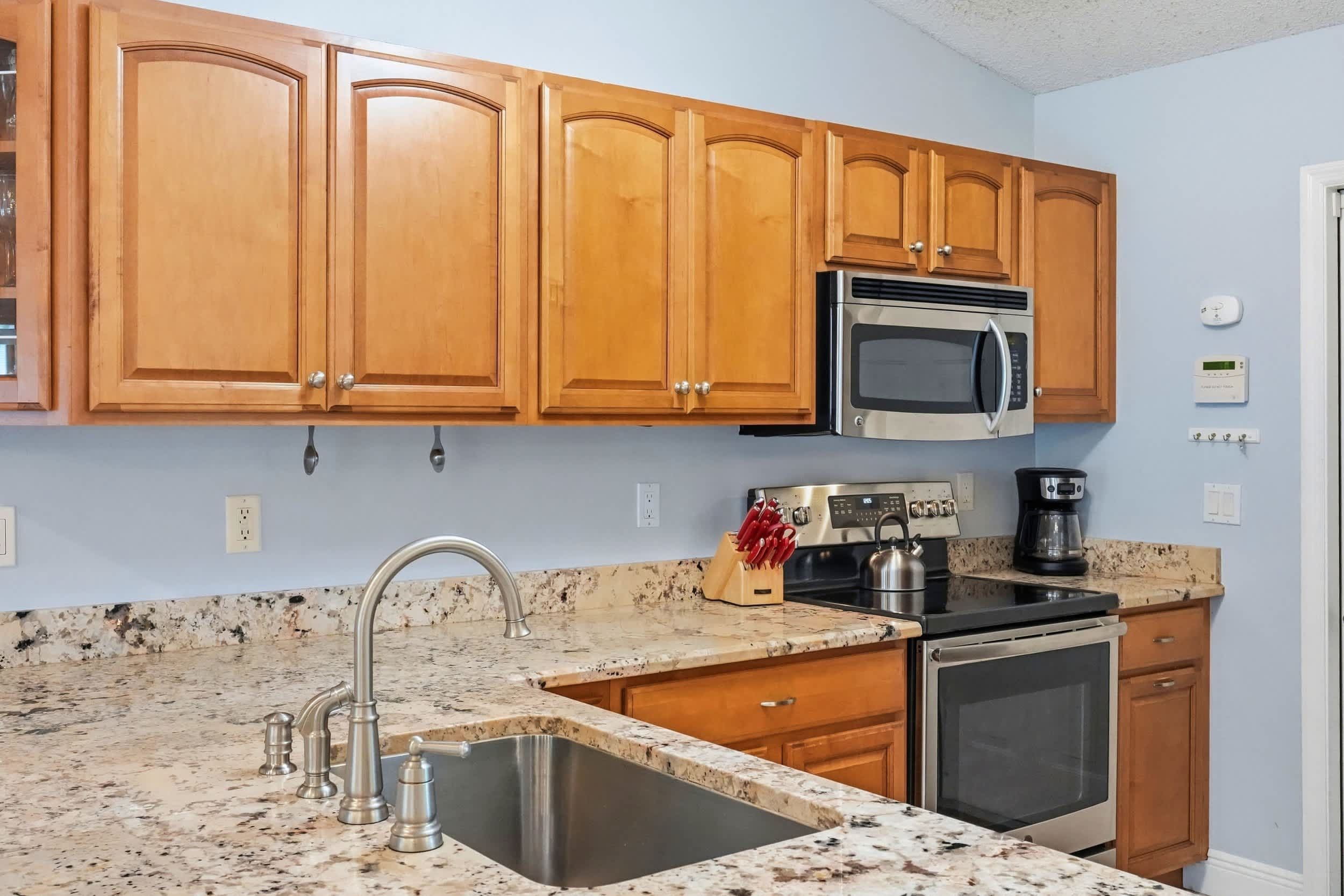 A kitchen with wooden cabinets, a stainless steel sink, a microwave, a kettle, and a coffee maker.