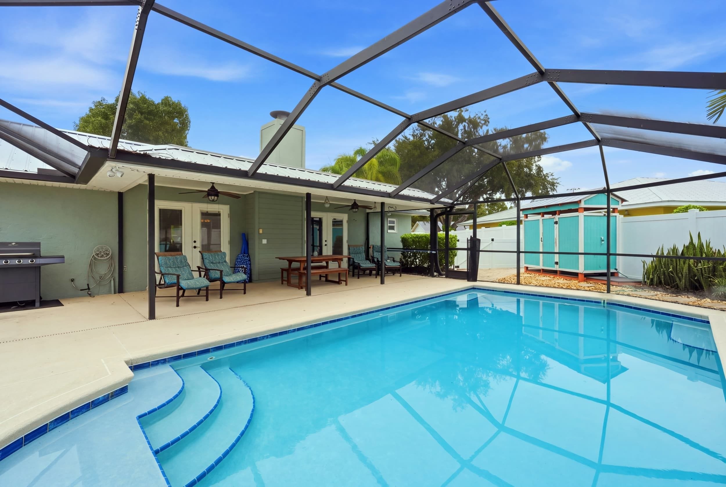 Une piscine extérieure couverte avec un espace patio comprenant des sièges et un barbecue.
