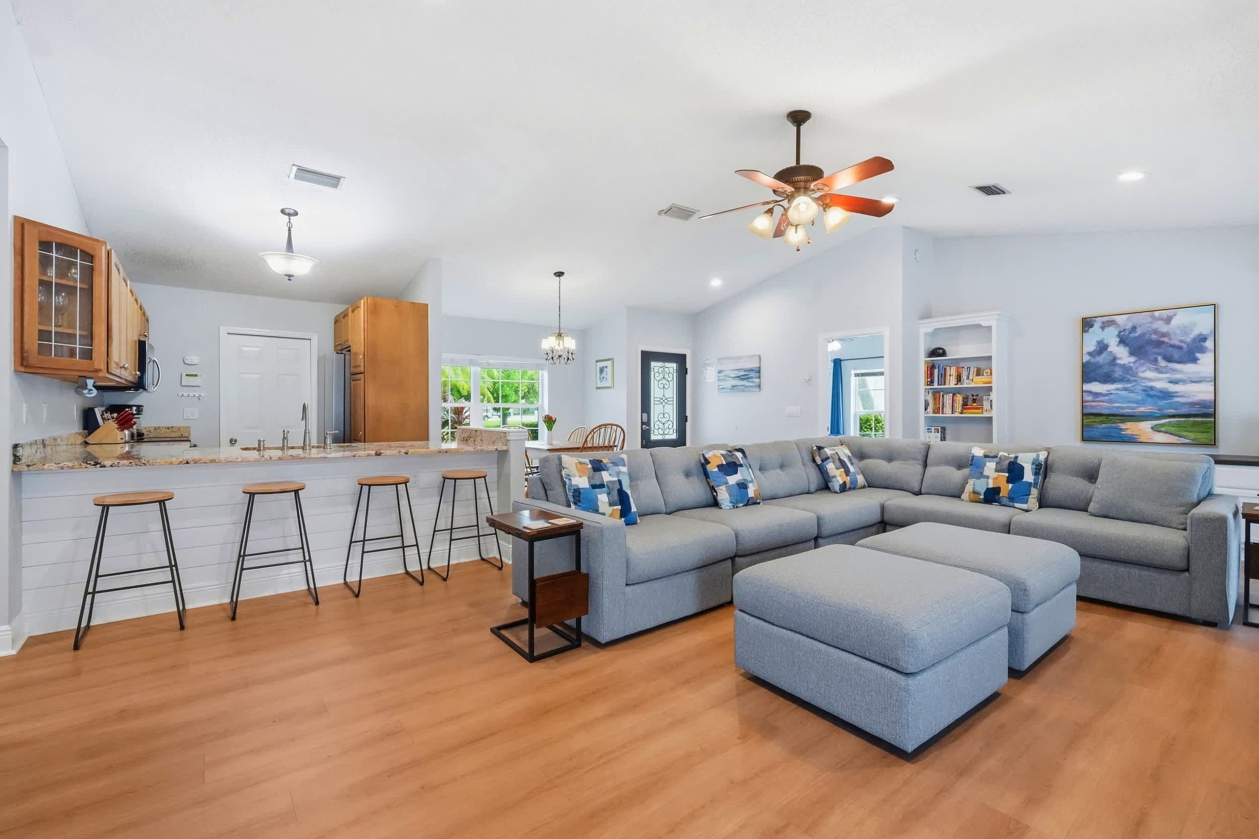 A modern living room with a sectional sofa, a bar area with stools, and a ceiling fan.