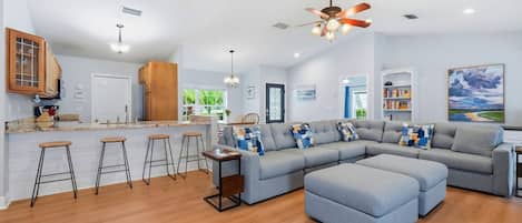 A modern living room with a sectional sofa, a bar area with stools, and a ceiling fan.