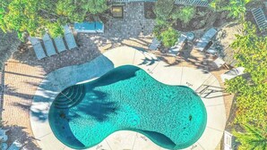 An aerial view of a swimming pool surrounded by lounge chairs and a brick pathway.