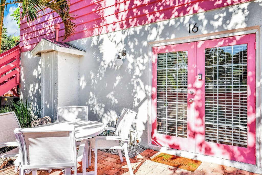 A pink building with a number 16, a patio with white chairs, and a door with a window.