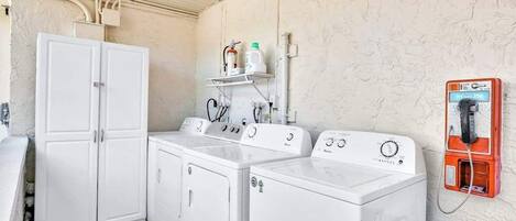 Un lavadero con lavadoras y secadoras blancas, una pared de servicios con un calentador de agua y un teléfono.