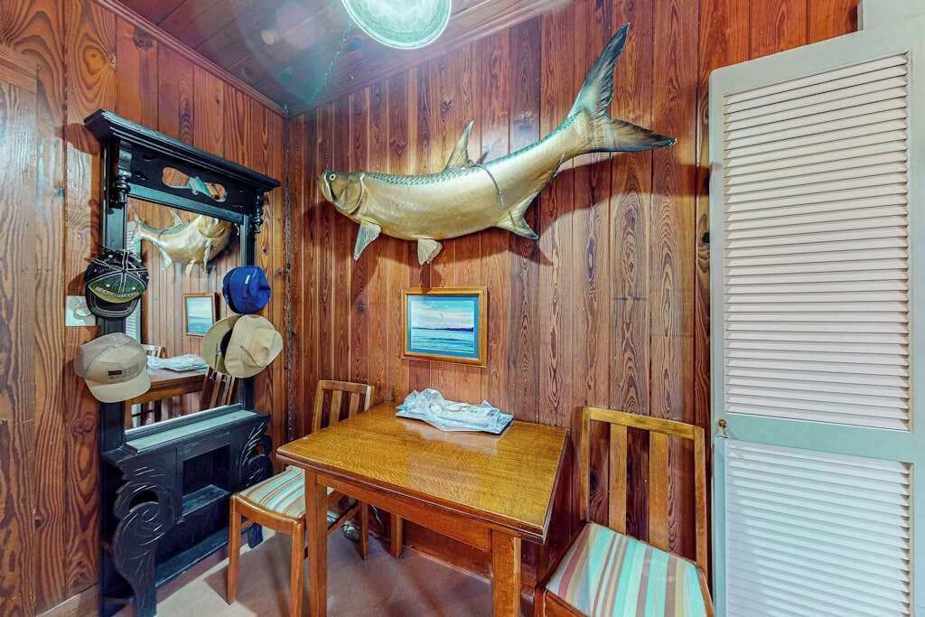 Une pièce aux murs lambrés, comprenant une table à manger, des chaises, un poisson empaillé accroché au mur et une cheminée.