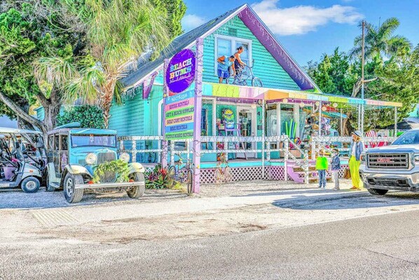 Un edificio colorido con un letrero que dice 'Beach Bums Rentals' y un porche cubierto.