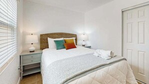 Un dormitorio con cama, lámparas de noche, una ventana con persianas y una puerta.