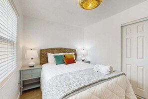 A bedroom with a bed, bedside lamps, a window with blinds, and a door.