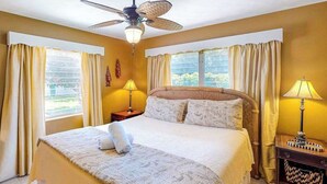 Un dormitorio con cama, ventilador de techo, dos lámparas de noche y cortinas.