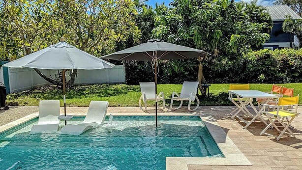 Una piscina con sillas de descanso y sombrillas, rodeada de follaje.