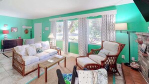 Un salón con sofá, sillón y mesa de centro, televisor y ventana con cortinas.