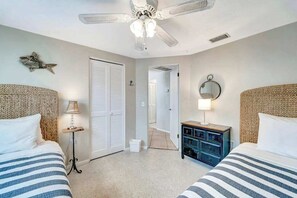 Ein Schlafzimmer mit zwei Betten, einem Deckenventilator, einem Nachttisch mit Lampe und einer Tür zu einem anderen Raum.
