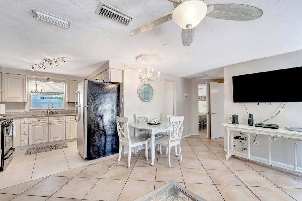 A modern kitchen with white cabinets, a black refrigerator, and a dining area with a glass table and white chairs.