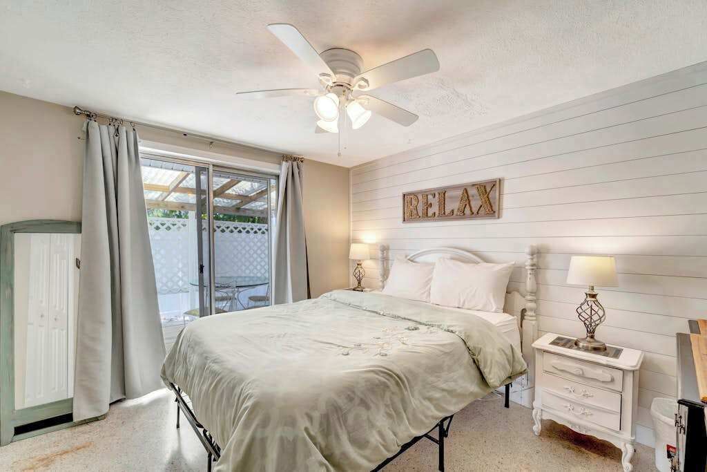 Un dormitorio con cama, ventilador de techo, mesita de noche con lámpara y un cartel que dice 'RELAX'.