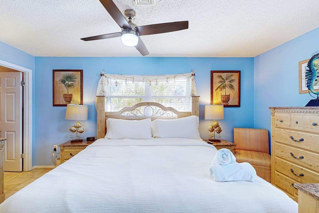 A bedroom with a bed, ceiling fan, bedside lamps, a dresser, and framed artwork on the walls.