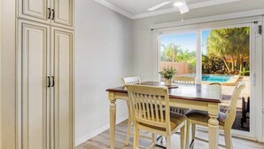 A dining area with a table and chairs, a ceiling fan, and a view of a swimming pool outside. - Charming Ground Floor Condo with Shared Pool, High-Speed WiFi, and Central AC (Holmes Beach)