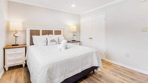 A bedroom with a bed, two bedside tables, a ceiling fan, and a white door. - Charming Ground Floor Condo with Shared Pool, High-Speed WiFi, and Central AC (Holmes Beach)
