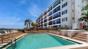 A swimming pool with a 6 FT depth, surrounded by a building with balconies and palm trees. - Waterfront condo with pool, internet & breathtaking balcony views (Sarasota)
