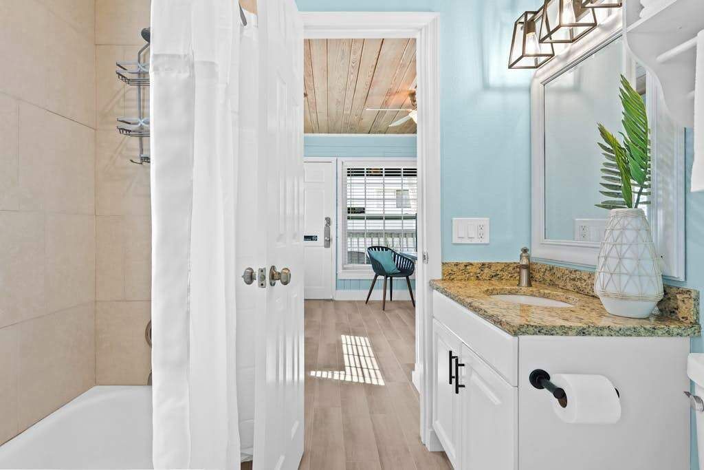Baño con ducha, lavamanos y espejo. Hay una puerta que da a otra habitación.