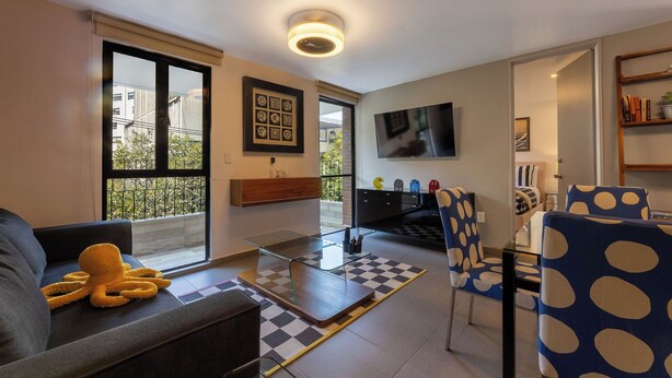 A modern living room with a sofa, a glass coffee table, a checkered rug, and a TV mounted on the wall. - Accommodation in Condesa with a balcony, within walking distance of Roma (Ciudad de México)