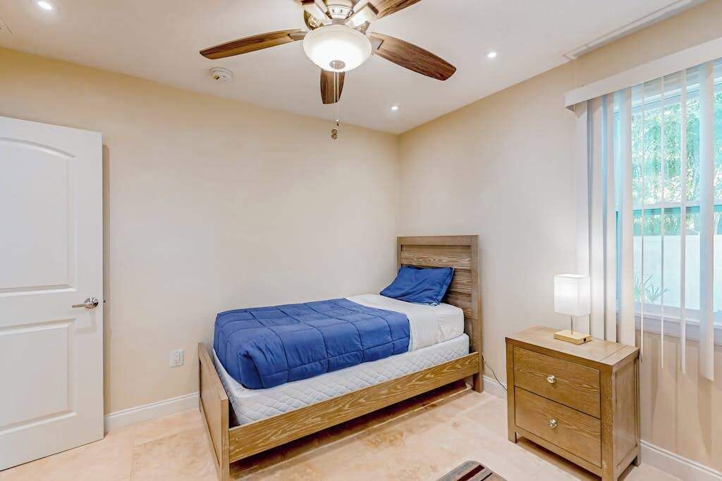Un dormitorio con cama, mesita de noche, ventilador de techo y ventana.