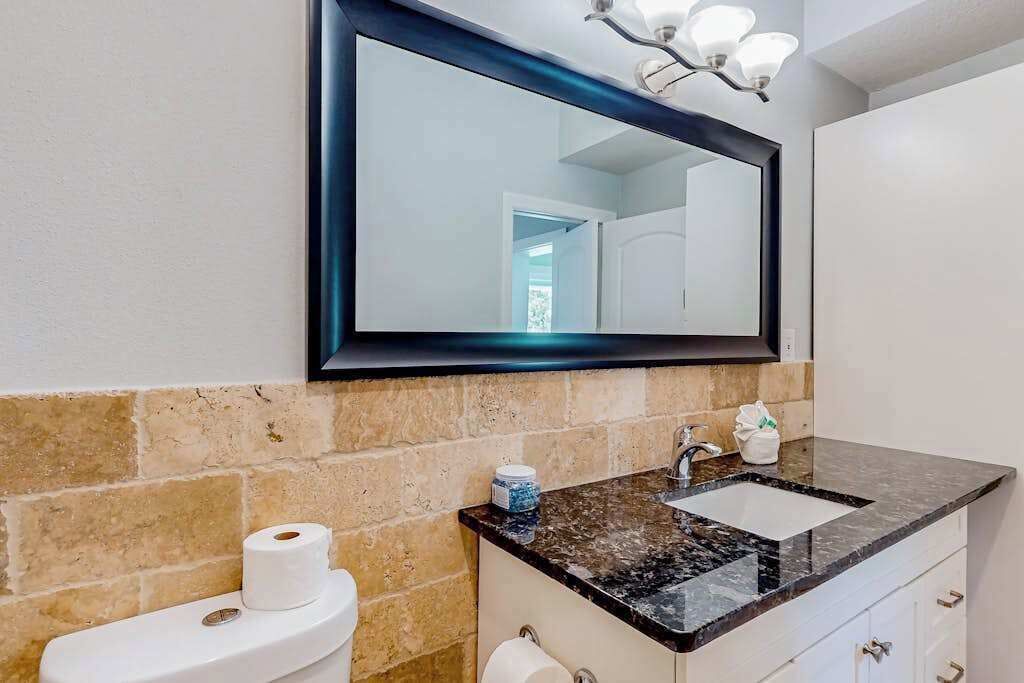 A bathroom with a marble sink, a toilet, a mirror, and a towel dispenser.