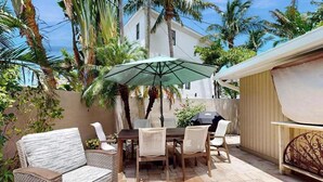 Eine Terrassengruppe im Freien mit Tisch, Stühlen und einem Korbsessel, sowie einem großen Sonnenschirm.