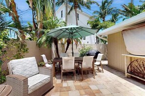 Eine Terrassengruppe im Freien mit Tisch, Stühlen und einem Korbsessel, sowie einem großen Sonnenschirm.