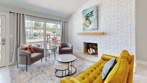 Ein Wohnzimmer mit weißer Ziegelwand, Kamin, gelbem Sofa und grauem Sofa.