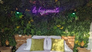 A bed with a green bedspread, two green pillows, and a neon sign above.