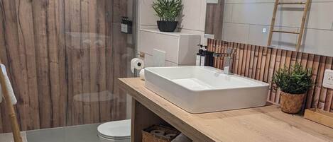 Une salle de bain moderne avec un meuble-lavabo en bois, un grand lavabo, des toilettes et un espace douche.