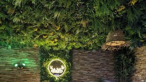 A spa area with two white chairs, a round table, a hot tub, and a wall with greenery and a neon sign.