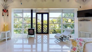 A spacious room with a large window, a bed, a TV, and a chair. - High-end home w heated private pool & spa, courtyard, & floor-to-ceiling windows (Anna Maria)
