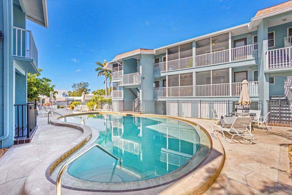 Zona de piscina con piscina curvo, sillas de descanso y un edificio con balcones.