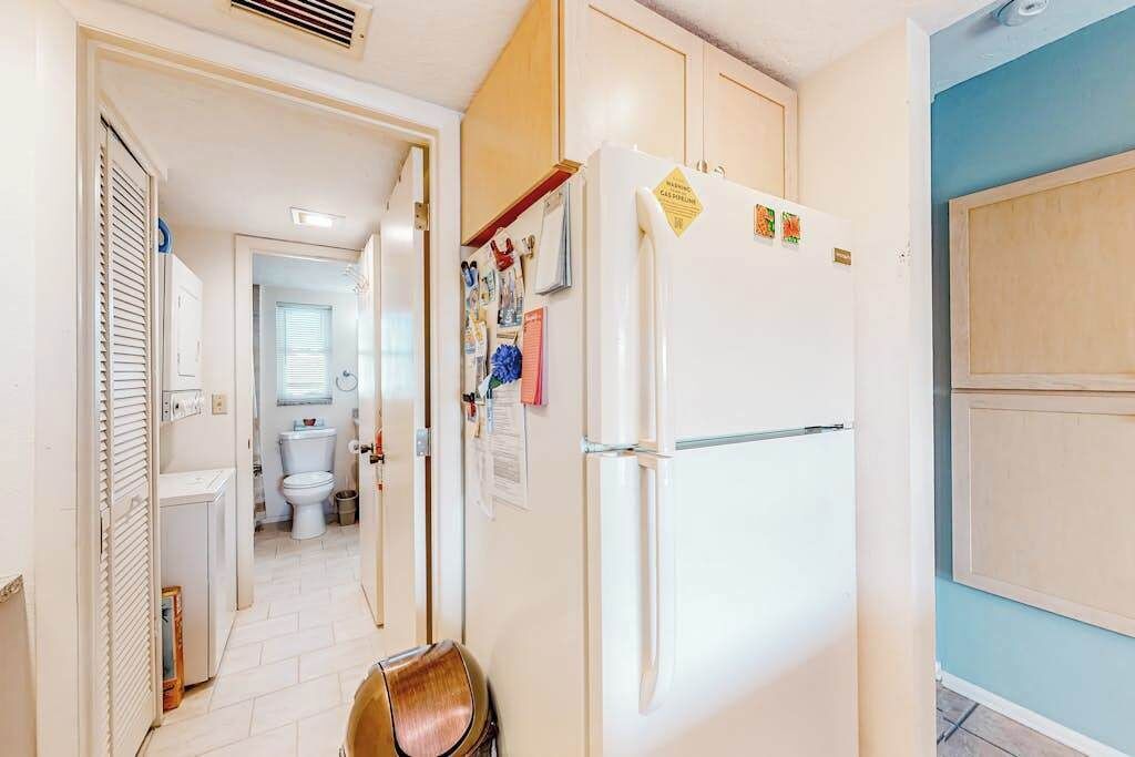 Un pasillo estrecho con un refrigerador blanco, una silla de madera y una puerta que da a un baño.