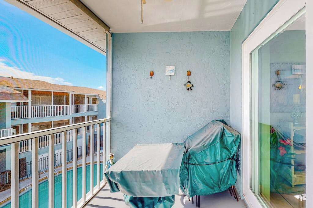 A balcony with a view of a building, a covered table, and a chair.