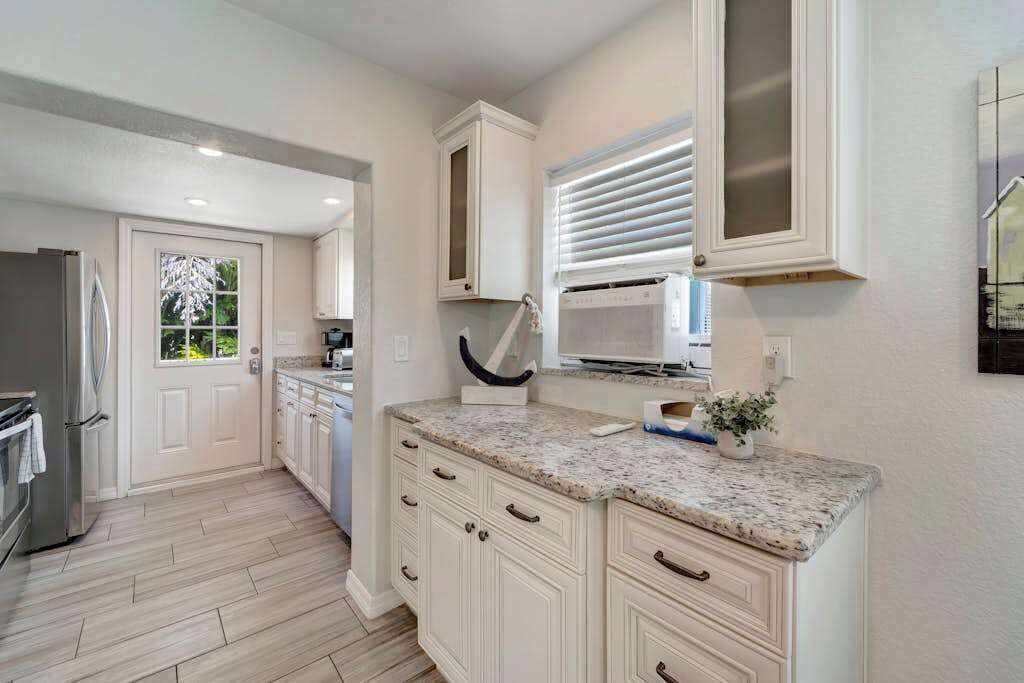 A kitchen with white cabinetry, a granite countertop, a microwave, and a window with blinds.
