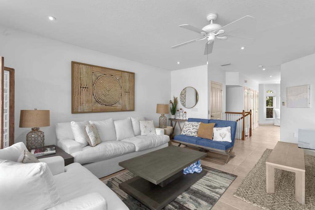 A modern living room with a white sofa, a blue sofa, a coffee table, and a ceiling fan.