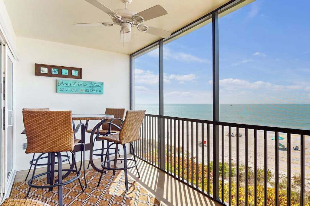 A balcony with wicker chairs, a table, a ceiling fan, and a sign reading 'Anna Maria Island.'