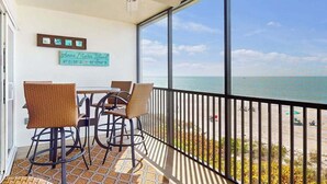 A balcony with wicker chairs, a table, a ceiling fan, and a sign reading 'Anna Maria Island.' - Oceanfront condo with WiFi, & ocean views, walk to free trolley (Bradenton Beach)