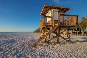 Una torre de salvavidas de madera en una playa arenosa con cielos despejados.