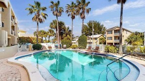 A swimming pool with a curved edge, surrounded by palm trees and residential buildings. - Oceanfront condo with WiFi, & ocean views, walk to free trolley (Bradenton Beach)