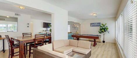 A spacious living area with a dining table, sofa, and a pool table.